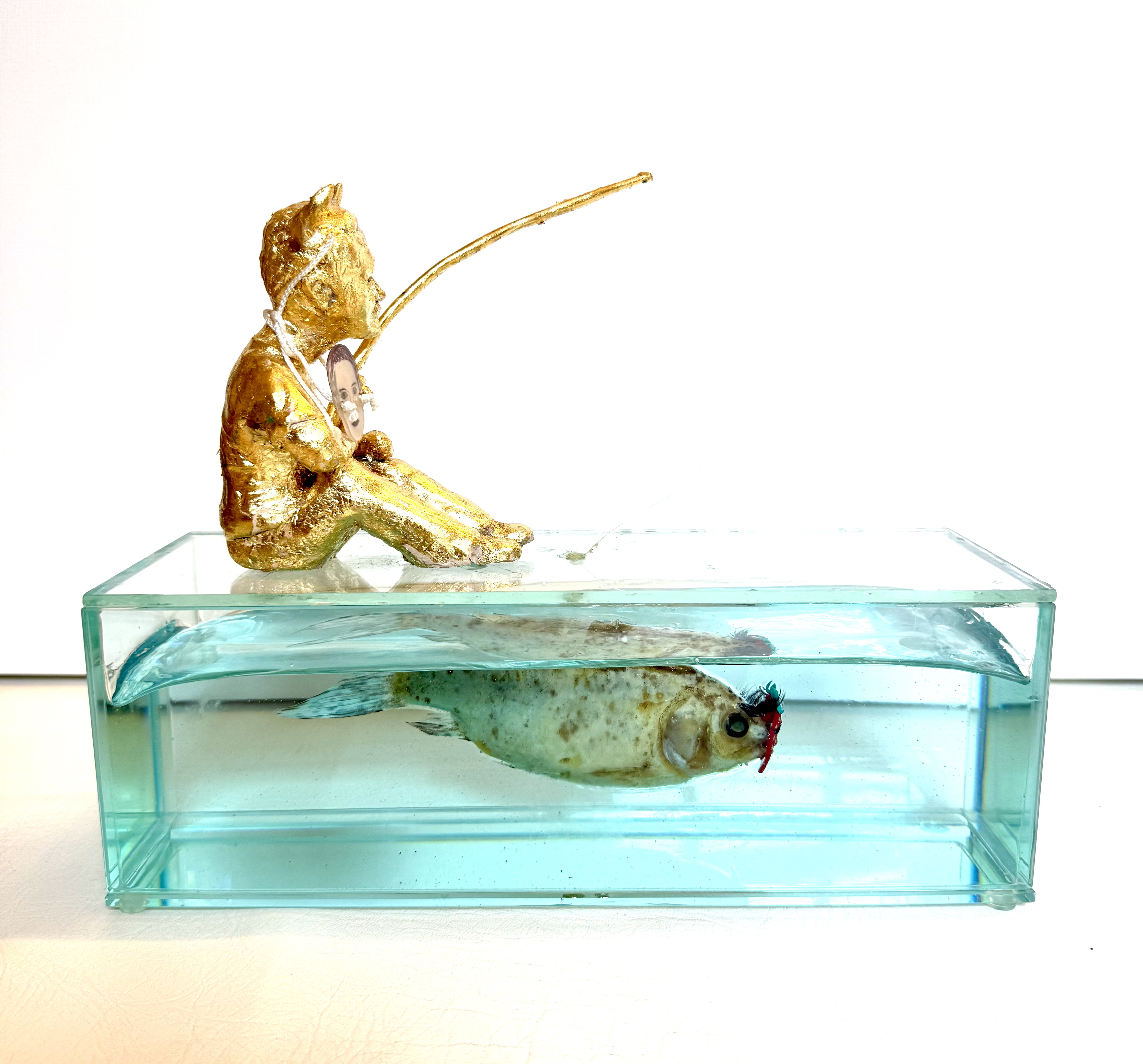Mark &mdash; gilded figure fishing atop a glass tank